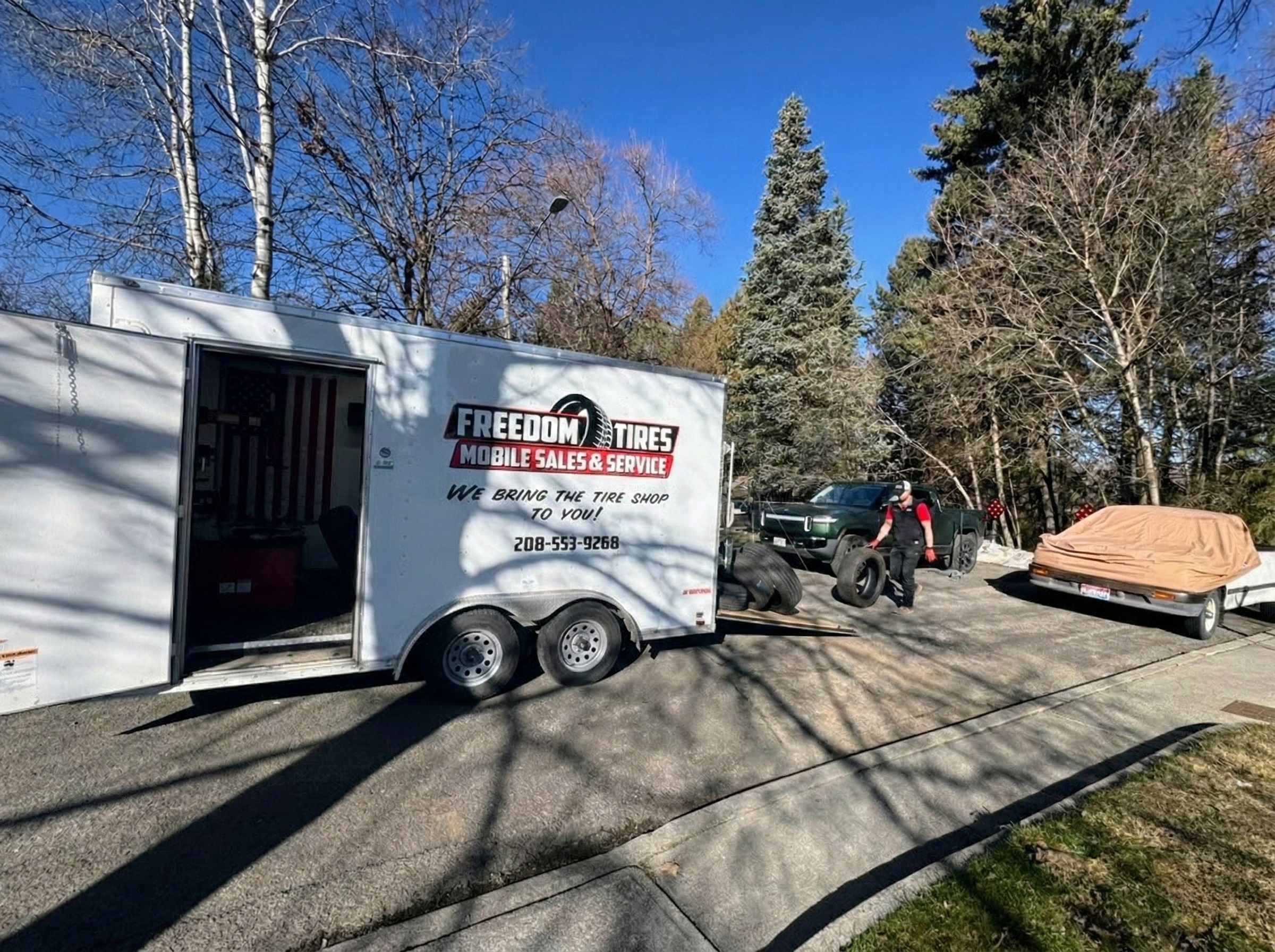 Freedom Tires trailer in residential driveway with operator rolling tires to vehicle