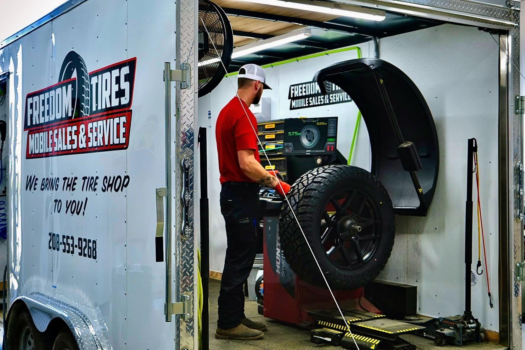 Freedom Tires operator at professional wheel balancer inside mobile trailer with branded exterior visible